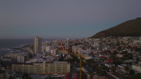 forwards-fly-above-city-at-twilight.-Multistorey-apartment-buildings-along-street-and-sea-in-background.-Cape-Town,-South-Africa