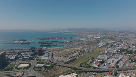 Aerial-shot-of-transport-infrastructure-in-city.-Elevated-multilane-highway,-railroad-tracks-and-harbour-on-waterfront.-Cape-Town,-South-Africa