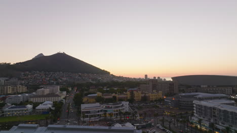 Backwards-reveal-of-buildings-in-shopping-and-entertainment-borough.-City-and-hills-against-sunset-sky.-Cape-Town,-South-Africa