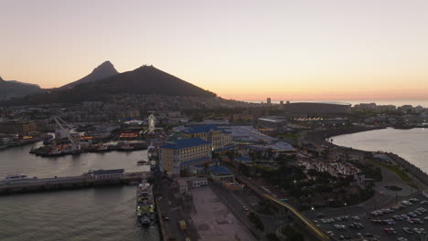 Aerial-footage-of-buildings-on-Victoria-and-Alfred-Waterfront-at-twilight.-Romantic-shot-of-shopping-and-entertaining-borough-in-city.-Cape-Town,-South-Africa