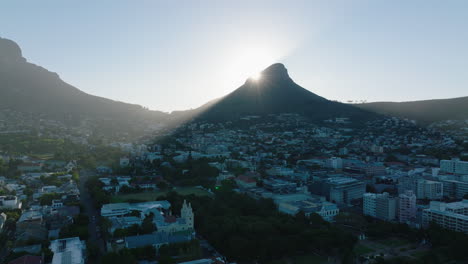 Diapositiva-Y-Toma-Panorámica-De-La-Cumbre-Puntiaguda-De-La-Montaña-De-Cabeza-De-León-Que-Se-Eleva-Sobre-La-Ciudad-Y-Proyecta-Sombra.-Ocultando-Gradualmente-El-Sol-Detrás-Del-Pico.-Ciudad-Del-Cabo,-Sudáfrica