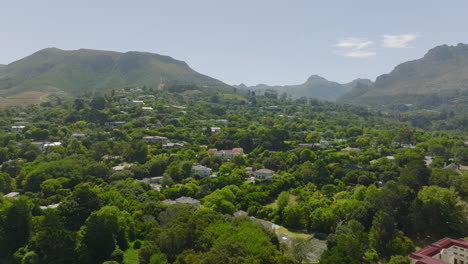 Aerial-footage-of-luxury-residences-surrounded-by-rich-lush-green-vegetation.-Large-houses-in-slope-between-trees.-Mountains-in-background.-Cape-Town,-South-Africa