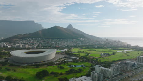 Slider-of-sport-venue-in-town-with-mountain-ridge-in-background.-Golf-course-and-modern-football-arena.-Cape-Town,-South-Africa