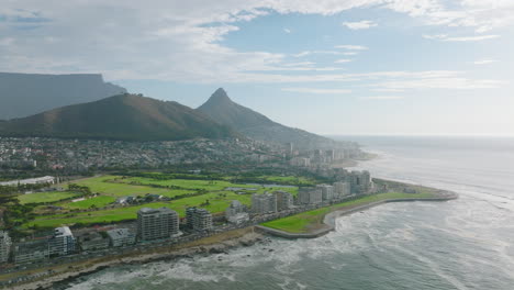 Aerial-panoramic-footage-of-Mouille-Point-borough-on-sea-coast.-Golf-course-and-futuristic-design-of-football-arena.-Mountain-s-in-background.-Cape-Town,-South-Africa