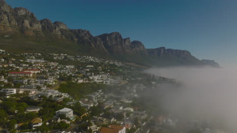 Static-shot-of-touristic-resort-at-seacoast-with-high-rocky-escarpment-in-background.-Morning-fog-rising-from-water-surface.-Cape-Town,-South-Africa