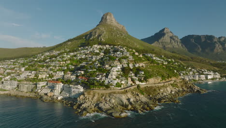 Forwards-fly-above-sea-coast.-Luxury-residences-and-apartments-on-sunny-slope-under-Lions-Head-mountain.-Cape-Town,-South-Africa