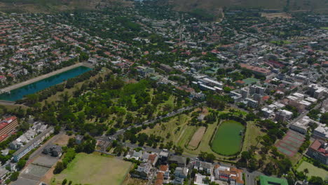 High-angle-view-of-De-Waal-Park-with-water-reservoirs-in-residential-suburb.-Tilt-up-reveal-mountains.-Cape-Town,-South-Africa