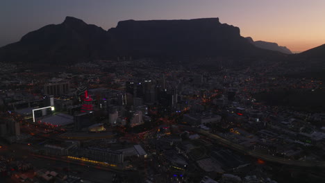 Aerial-view-of-urban-borough-at-night.-Mountain-range-against-colourful-twilight-sky-in-background.-Cape-Town,-South-Africa