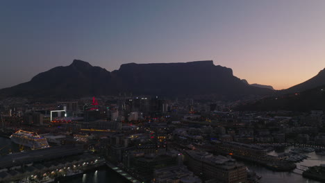 Forwards-fly-above-evening-city.-Table-Mountain-massif-against-sky-in-background.-Cape-Town,-South-Africa