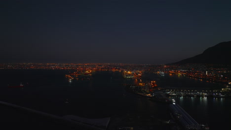 Aerial-panoramic-night-city-scene.-Fly-above-waterfront-with-view-of-marina-and-harbour.-Cape-Town,-South-Africa