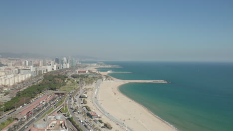Aerial-footage-of-sand-beach-along-sea-coast-in-city.-Traffic-on-roads-around.-Sunny-day-in-travel-destination.-Barcelona,-Spain