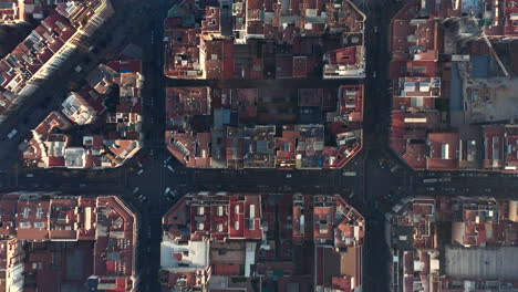 Top-down-shot-of-blocks-of-residential-buildings-in-urban-borough-at-golden-hour.-Revealing-part-of-unfinished-basilica-Sagrada-Familia.-Barcelona,-Spain