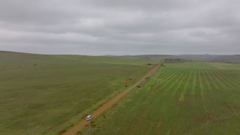 Aerial-view-of-car-driving-on-dirt-road-in-agricultural-countryside.-Cloudy-day-in-landscape.-South-Africa