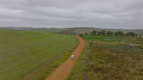 Slowly-driving-van-on-dusty-path-in-landscape-on-cloudy-day.-Car-passing-between-agricultural-fields.-South-Africa
