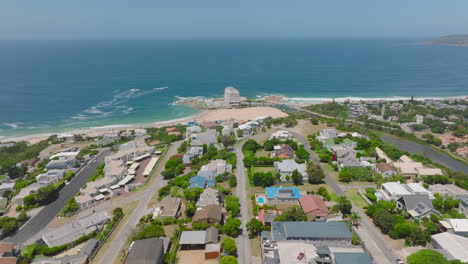 Aerial-ascending-footage-of-urban-borough-high-above-sea-coast.-Sand-beach-and-sea-surface-in-background.-Plettenberg-Bay,-South-Africa