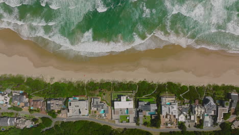 Aufnahmen-Von-Oben-Nach-Unten-Auf-Gebäude-Entlang-Der-Meeresküste-Schwenken.-Erstaunliche-Aufnahme-Von-Wellen,-Die-Zum-Sandstrand-Rollen.-Südafrika