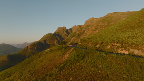 Aerial-view-of-road-traversing-mountain-landscape-lit-by-bright-sun-in-golden-hour.-Cars-standing-on-lookout-point.-South-Africa