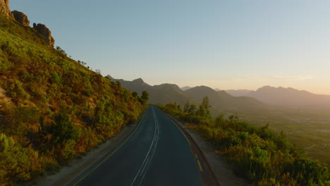 Car-driving-on-road-in-mountains.-Morning-or-evening-light-in-golden-hour.-Forwards-fly-above-road.-South-Africa