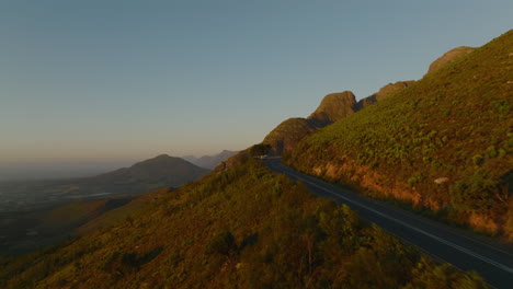 Forwards-fly-along-road-in-mountains.-Travellers-standing-at-lookout-point-and-watching-sunset.-South-Africa