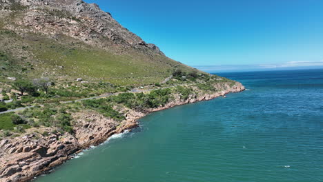 Fly-along-sea-coast-in-tropical-destination.-Step-rocky-slope-rising-from-turquoise-water-on-sunny-day.-South-Africa