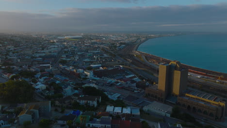 Fly-around-high-rise-post-office-building-lit-by-setting-sun.-Aerial-footage-of-city-at-sea-bay.-Port-Elisabeth,-South-Africa