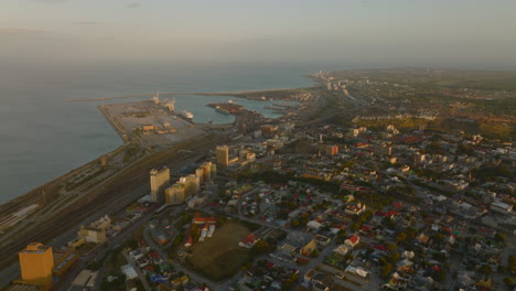 Forwards-fly-above-city-at-sunset.-Aerial-view-of-urban-neighbourhood-and-harbour-on-sea-coast.-Port-Elisabeth,-South-Africa