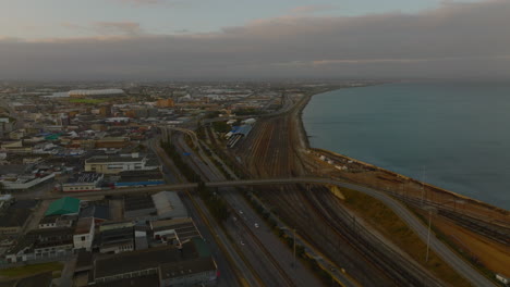 Highway-and-railway-leading-along-sea-coast.-Aerial-view-of-transport-infrastructure-in-city-at-dusk.-Port-Elisabeth,-South-Africa