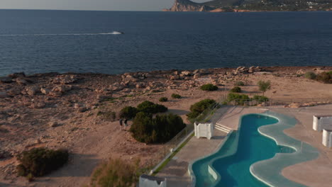 Establisher-Aufnahme-Eines-Leeren-Swimmingpools-Im-Resort-Mit-Zwei-Personen,-Die-Die-Straße-Hinuntergehen,-Mit-Blick-Auf-Eine-Nicht-Erkannte-Person,-Die-Wassersportarten-Auf-Ibiza-In-Spanien-Genießt