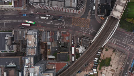 Aerial-birds-eye-overhead-top-down-panning-view-of-traffic-in-streets-in-urban-neighbourhood.-Elevated-double-track-railway-leading-across-roads.-London,-UK