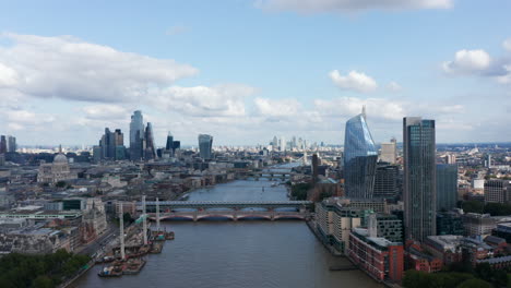 Backwards-fly-above-Thames-river.-Aerial-panoramic-view-of-city-with-modern-dominants.-Building-in-City-financial-hub-and-One-Blackfriars-skyscraper-with-reflecting-sky.-London,-UK
