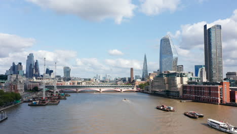 Fly-above-Thames-river-at-Blackfriars-bridges.-Boats-floating-on-water-surface.-Tall-modern-buildings-towering-above-the-surrounding-buildings.-London,-UK
