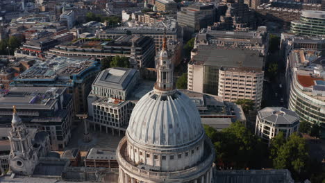 Fly-over-dome-of-historic-Saint-Pauls-Cathedral-in-afternoon-bright-sun.-Tilt-down-on-decorated-tower-with-cross-on-top.-London,-UK