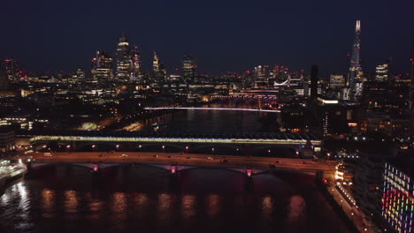 Forwards-fly-above-Thames-river-at-night.-Aerial-view-of-colourful-city-lights-glowing-into-dark.-London,-UK