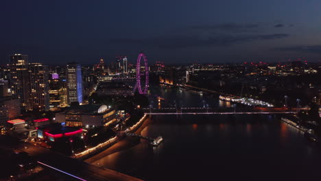 Luftaufnahme-Der-Stadt-Nach-Sonnenuntergang.-Nachtflug-über-Themse,-Beleuchtete-Brücken-Und-Violettes-London-Eye.-London,-Vereinigtes-Königreich