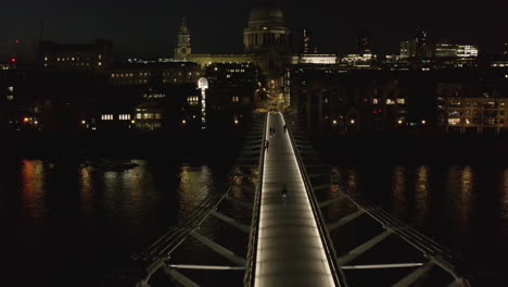 Fly-above-modern-designed-Millennium-Footbridge-across-Thames-river.-Tilt-up-reveal-of-Saint-Pauls-Cathedral.--London,-UK