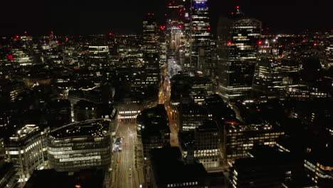 Tilt-up-reveal-of-tall-modern-buildings,-skyscrapers-in-City-business-district.-Aerial-view-of-city-at-night.-London,-UK