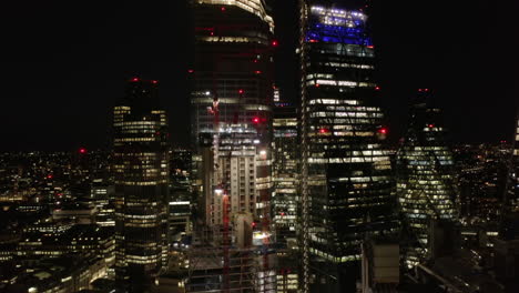 Backwards-reveal-of-skyscrapers-in-City-financial-district.-Pull-back-footage-of-brightly-illuminated-construction-site-with-tower-cranes.-London,-UK