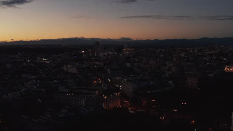 Fly-above-evening-city.-Panoramic-aerial-view-of-dimmed-town-under-colourful-twilight-sky.