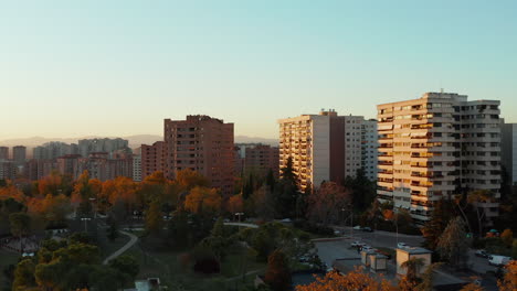 Autumn-afternoon-at-housing-estate-in-city.-Forwards-fly-above-colourful-trees-in-park.-Apartment-buildings-lit-by-setting-sun.