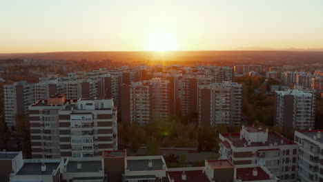 Fly-above-housing-estate,-revealing-multistorey-prefabricated-apartment-buildings.-Aerial-view-against-setting-sun.