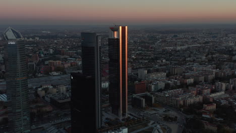 Descending-aerial-footage-of-futuristic-tall-skyscrapers-in-Cuatro-Torres-Business-area-at-dusk.-Glossy-facade-reflecting-colourful-twilight-sky.