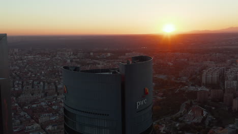 Fly-around-top-of-PWC-tower-in-Cuatro-Torres-Business-area.-Modern-high-rise-office-building.-View-against-setting-sun.
