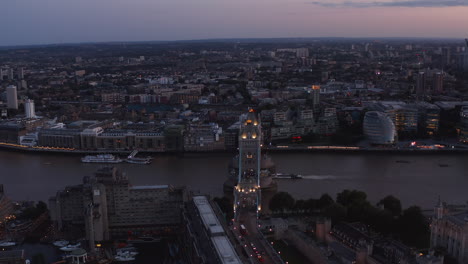 Slide-and-pan-aerial-footage-of-traffic-on-Thames-river-water-surface.-Boat-floating-under-illuminated-Tower-Bridge-after-sunset.-London,-UK