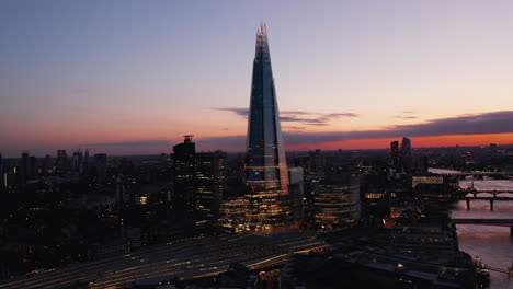 Amazing-evening-elevated-footage-of-modern-skyscraper-on-River-Thames-south-bank.-Tall-The-Shard-after-sunset.-London,-UK