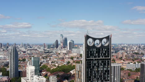 Forwards-fly-around-modern-skyscraper-with-wind-turbines-in-top-part-of-construction.-Revealing-panoramic-view-of-city-with-group-of-tall-office-buildings.-London,-UK