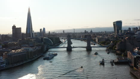 Tower-Bridge-over-River-Thames.-Backwards-reveal-of-buildings-on-waterfronts.-View-against-sunshine.-London,-UK