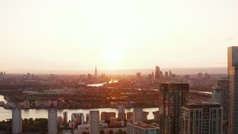 Fly-over-top-platform-of-Arena-Tower-apartment-complex.-Panoramic-view-of-Thames-river-winding-through-large-city.-Cityscape-against-sunset.-London,-UK