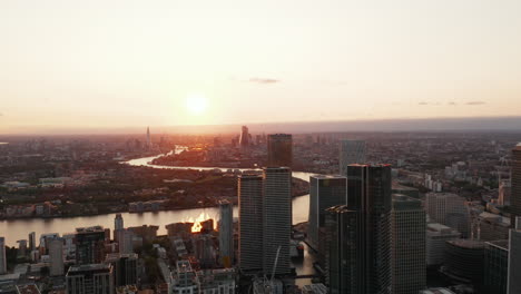 Backwards-reveal-of-modern-tall-buildings-in-Canary-Wharf-business-district.-Aerial-panoramic-footage-against-sunset.-London,-UK