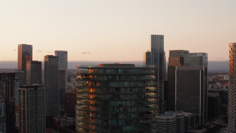 Slide-and-pan-footage-of-top-of-Baltimore-Tower.-Cylindrical-apartment-building-with-terraces-on-rings-around.-Skyscrapers-in-Canary-Wharf-borough-and-cityscape-in-sunset-time.-London,-UK