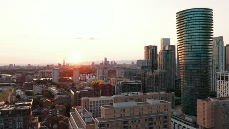 Descending-footage-of-residential-buildings-on-Isle-of-Dogs-next-by-skyscrapers-in-Canary-Wharf.-View-against-setting-sun.-London,-UK